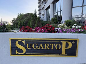 A sign for 'Sugarto' with a modern building in the background.