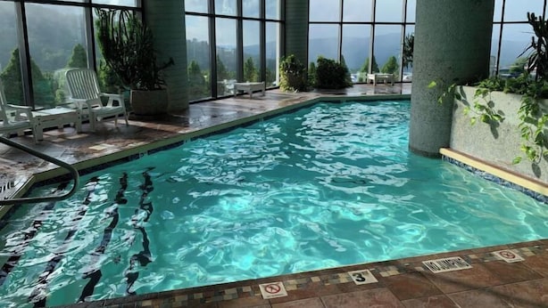 Una piscina interior con agua cristalina, rodeada de amplios ventanales con vistas a la ciudad y las montañas.