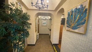 Un pasillo con pared texturizada, un candelabro, una obra de arte enmarcada y una planta en maceta.
