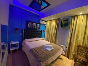 Ein Schlafzimmer mit Bett, Sessel, Fernseher und einem Fenster mit Vorhängen.