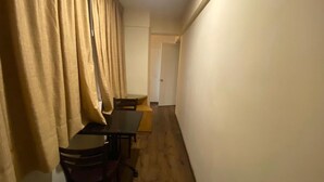 Un pasillo estrecho con suelo de madera, una mesa con sillas y una puerta al final.