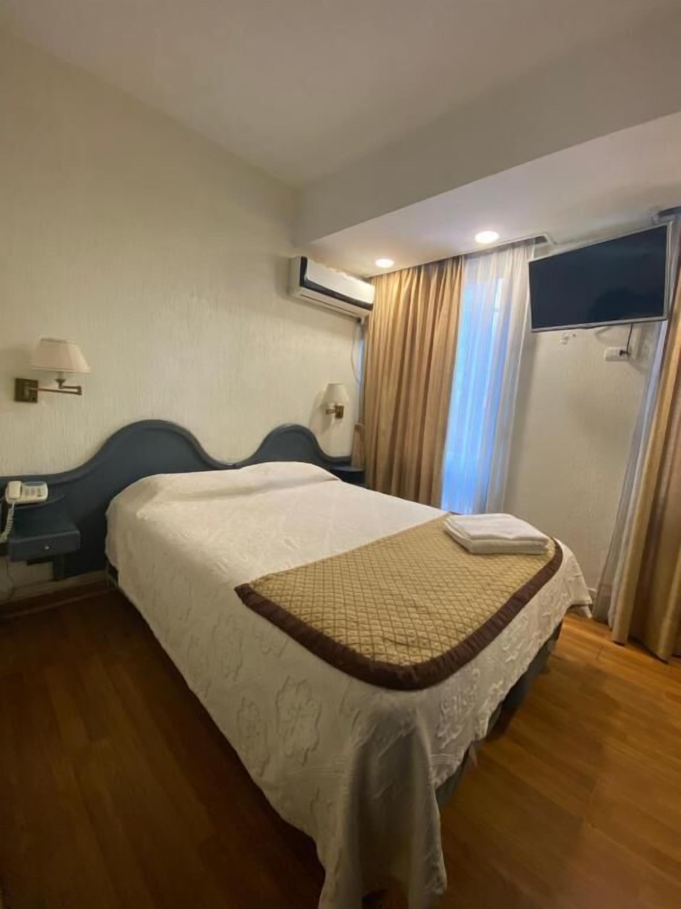 Ein Hotelzimmer mit Bett, Nachttischen, Telefon, Klimaanlage und Vorhängen.