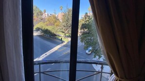 Vista desde una ventana con cortinas, que da a una calle con edificios y árboles.