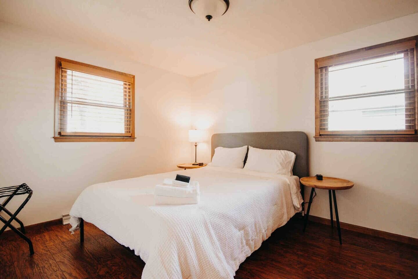 Een keurig opgemaakte slaapkamer met een bed, nachtkastjes en twee ramen met jaloezieën.