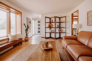 A cozy living room with a leather sofa, wooden floor, and a built-in bookshelf with decorative items. - RIVER RETREAT, River Retreat, Fenced Backyard, Peaceful (River Falls)
