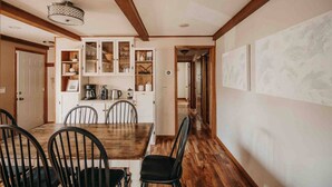 A dining area with a wooden table and chairs, a kitchen with cabinets and appliances, and a hallway with artwork on the walls. - RIVER RETREAT, River Retreat, Fenced Backyard, Peaceful (River Falls)