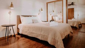 A spacious bedroom with a large bed, bedside lamps, a round table, and a mirror. - RIVER RETREAT, River Retreat, Fenced Backyard, Peaceful (River Falls)