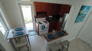Een compacte keuken met een kookplaat, oven en houten kastjes. Er staan twee eettafels met stoelen en een klein vloerkleed.