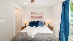 A bedroom with a bed, two bedside tables with lamps, a window with blue curtains, and a wall-mounted artwork. - Quiet Mountain Home with Fireplace, A+ location! (Banner Elk)