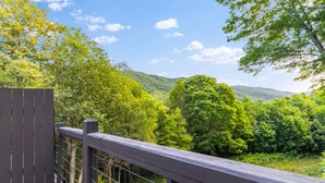 A wooden deck with a metal railing overlooking a lush, green forested valley. - Quiet Mountain Home with Fireplace, A+ location! (Banner Elk)