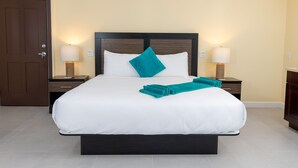 A hotel room with a large bed, two bedside tables with lamps, a wooden door, and a light-colored wall. - The New View Inn (Road Town)