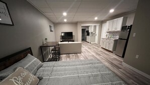 A bedroom with a bed, a desk, and a kitchenette in the background. - The Studio Above the Studio (Jackson)