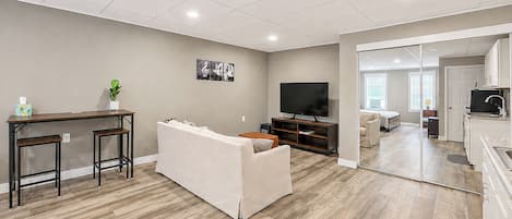 A modern living room with a sofa, a TV, and a dining area with stools.
