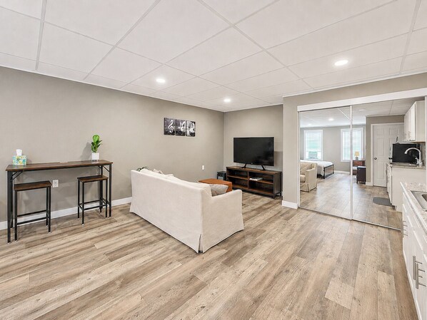 A modern living room with a sofa, a TV, and a dining area with stools.