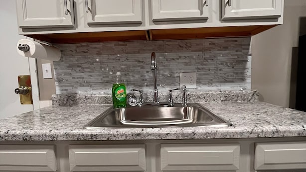 A kitchen with white cabinets, a granite countertop, and a stainless steel sink. - The Studio Above the Studio (Jackson)