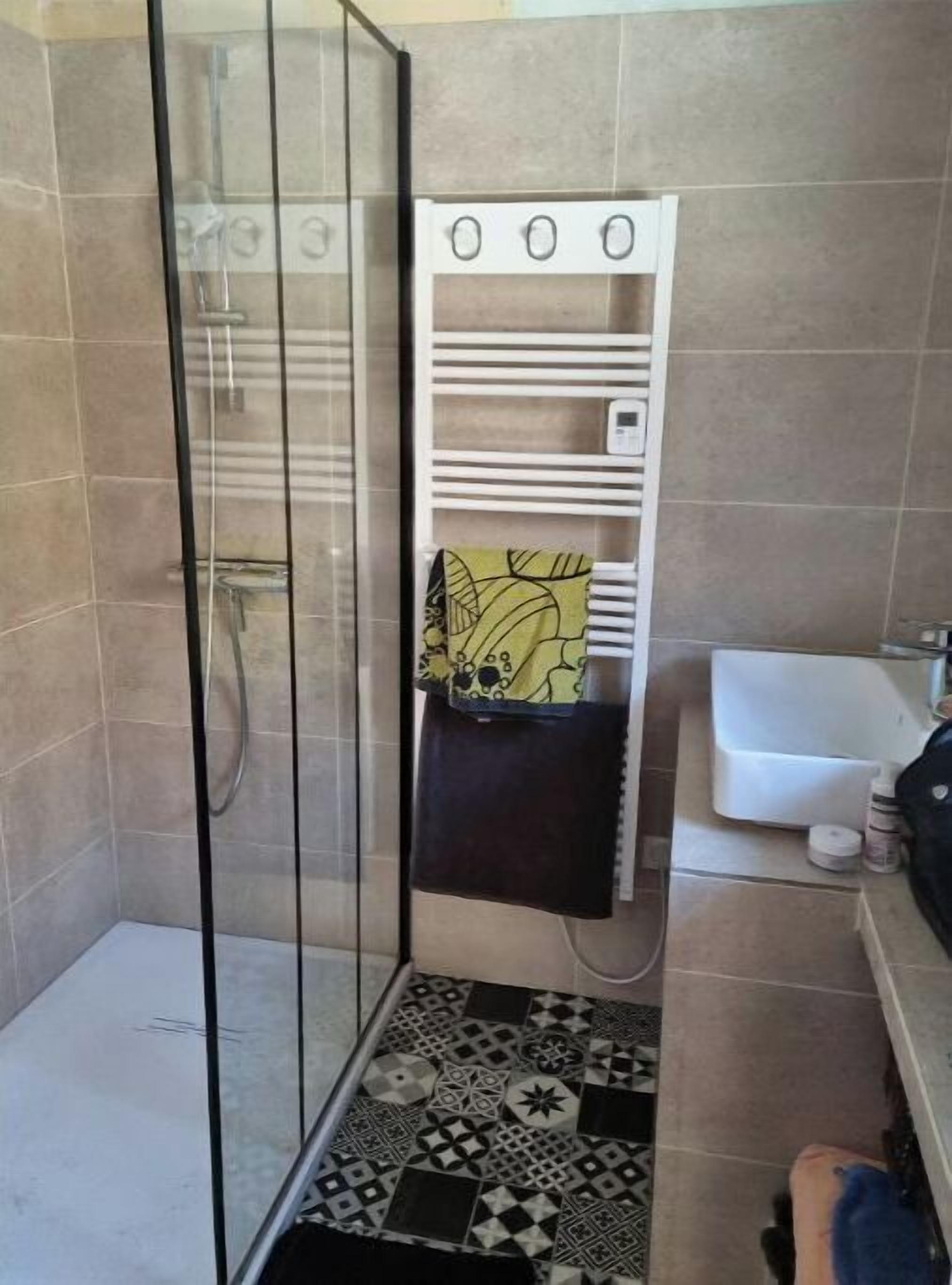 A bathroom with a glass shower enclosure, a white sink, and a patterned floor.