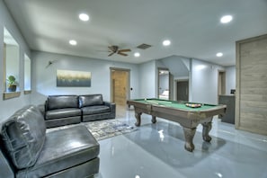 A modern living room with a pool table, leather sofa, and a ceiling fan.