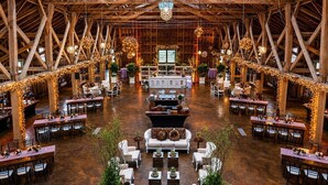 Une vaste salle dotée de hauts plafonds et de poutres en bois, comprenant plusieurs tables à manger et des coins salon.