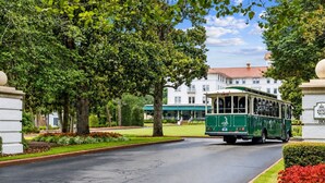 A green trolley on a paved road, a building with a red roof, and a well-maintained lawn. - Legends & Masters | Walk to Pinehurst Clubhouse | Hallmark-Style Charm (Pinehurst)