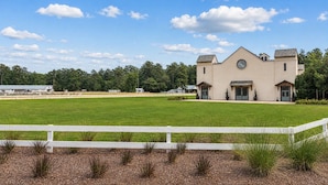 A large building with a symmetrical facade, a central circular window, and a white fence in the foreground. - Legends & Masters | Walk to Pinehurst Clubhouse | Hallmark-Style Charm (Pinehurst)