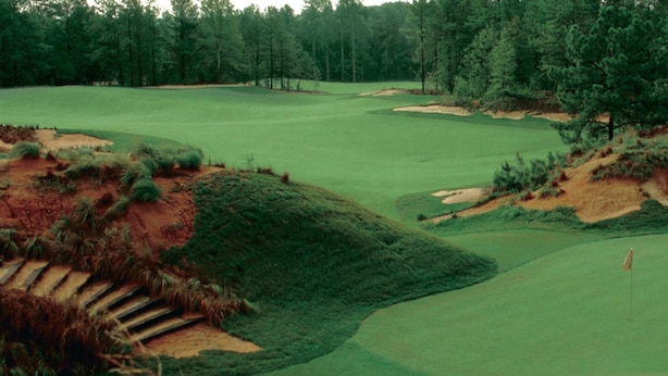 A golf course with sand bunkers, a flagstick, and a wooded area in the background. - Legends & Masters | Walk to Pinehurst Clubhouse | Hallmark-Style Charm (Pinehurst)