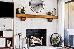 A living room with a white brick fireplace, a wooden mantel, and a round mirror above it. - Legends & Masters | Walk to Pinehurst Clubhouse | Hallmark-Style Charm (Pinehurst)