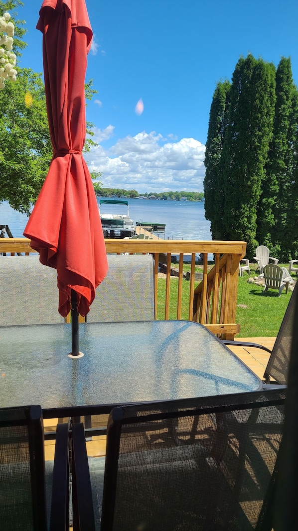 Una mesa con un paraguas rojo, vistas a un lago y una terraza de madera con sillas.