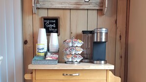 A wooden cabinet with a coffee station, including a coffee maker, sugar, and creamer.