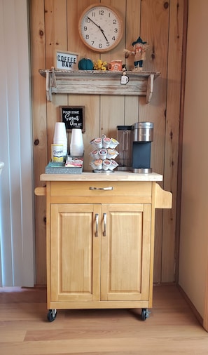 Un mueble de madera con una estación de café, que incluye una cafetera, azúcar y crema.