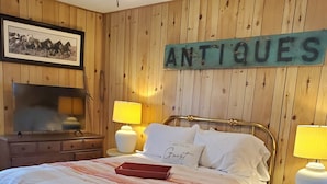 A wooden-paneled room with a bed, two bedside lamps, a framed picture, and a sign that reads "ANTIOQUES".