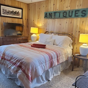 Una habitación con paneles de madera, una cama, dos lámparas de noche, un cuadro enmarcado y un letrero que dice "ANTIOQUES".