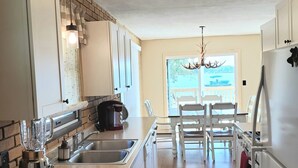 A kitchen with a brick accent wall, white cabinetry, a built-in island with a sink, a coffee maker, and a chandelier.