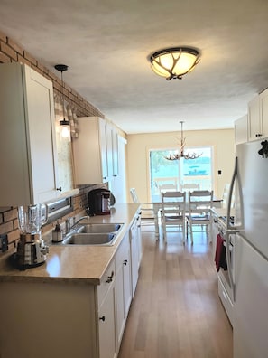 Una cocina con pared de ladrillo decorativa, armarios blancos, una isla integrada con fregadero, cafetera y candelabro.