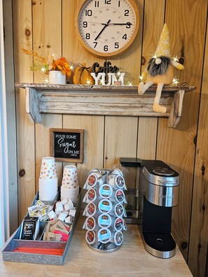 A coffee station with a clock, a sign that says 'Pour Some Sugar On Me,' and a coffee machine.