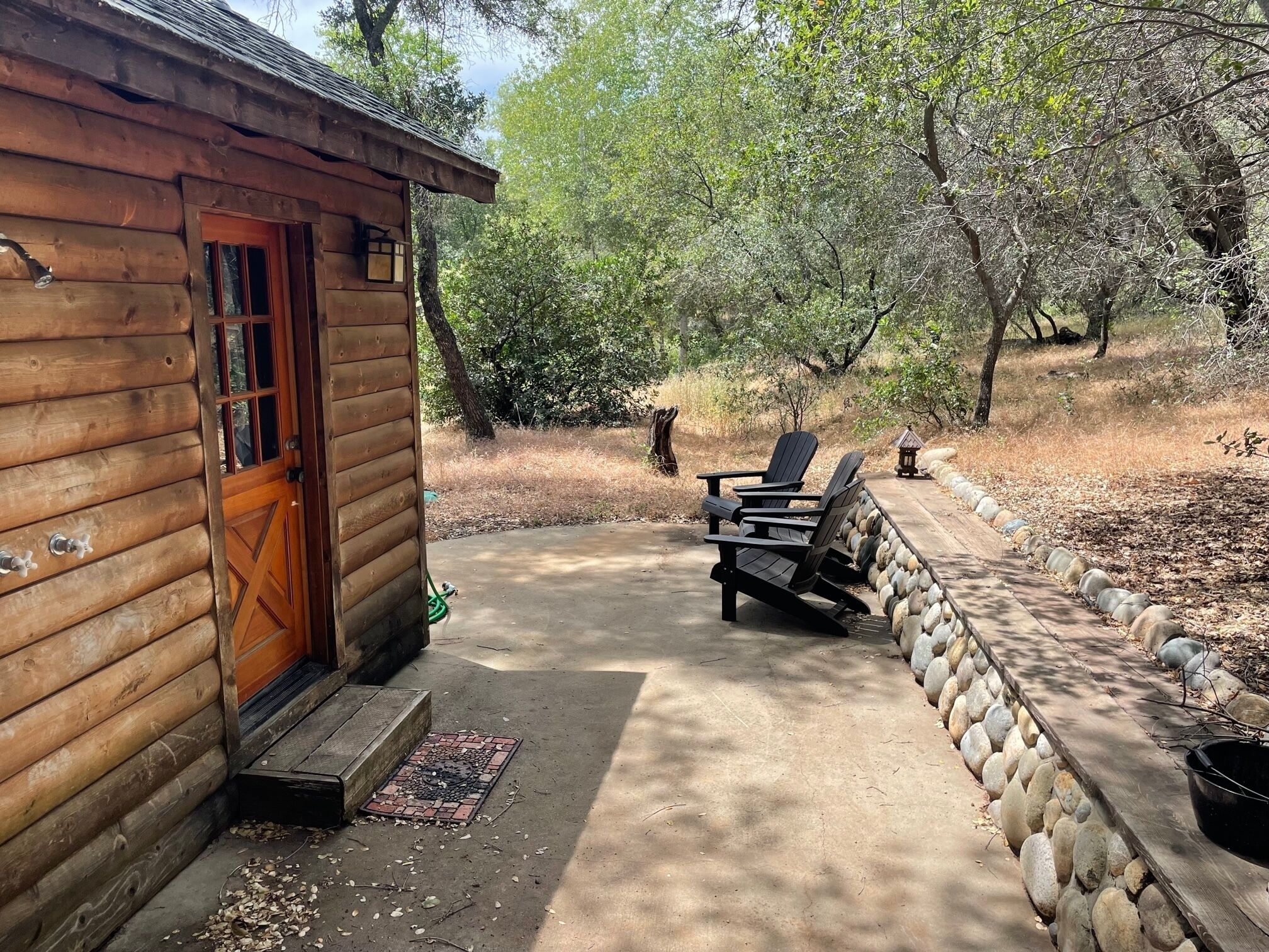 A wooden cabin with a door, a concrete patio, and two Adirondack chairs.