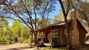 A rustic cabin with a stone chimney, wooden exterior, and a porch with outdoor seating. - Duck Pond Cabin-Private Cabin on 400 Acre Ranch (Smartsville)