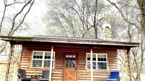 A rustic cabin with a wooden exterior, a front porch with two chairs, and a stone chimney. - Duck Pond Cabin-Private Cabin on 400 Acre Ranch (Smartsville)