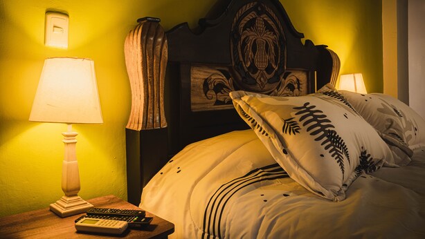 A bed with a wooden headboard, a nightstand with a lamp, and a wall-mounted light switch. - SD-1 HABITACION EN LA CIUDAD ANTIGUA (Cartagena)