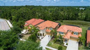 A residential area with multiple houses featuring red-tiled roofs and beige walls, surrounded by lush greenery and a clear sky. - Contemporary 6 Bed 6 Bath Luxury Villa at Watersong (Davenport)
