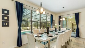 A dining area with a long table, white chairs, and a chandelier. - Contemporary 6 Bed 6 Bath Luxury Villa at Watersong (Davenport)
