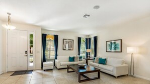 A living room with two white sofas, a coffee table, a floor lamp, and a door with a doormat. - Contemporary 6 Bed 6 Bath Luxury Villa at Watersong (Davenport)