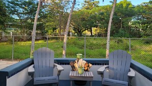 Een terras met twee Adirondack-stoelen, een kleine tafel met een plant en houtblokken, en een witte kussen.