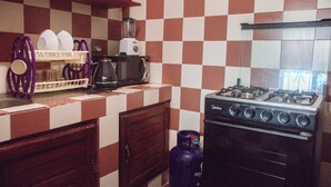 Una cocina con salpicadero de baldosas a cuadros, una estufa a gas, una licuadora y un escurreplatos con tazas.