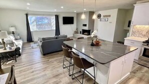 Una cocina moderna con una isla central, un comedor con mesa y sillas, un sofá y una chimenea.