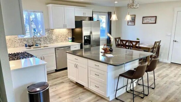 Una cocina moderna con armarios blancos, un refrigerador de acero inoxidable y una isla central con taburetes de bar.
