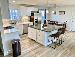 A modern kitchen with white cabinets, a stainless steel refrigerator, and a central island with bar stools. - Hometown USA With Hot Tub and Fully Renovated (Mountain Home)