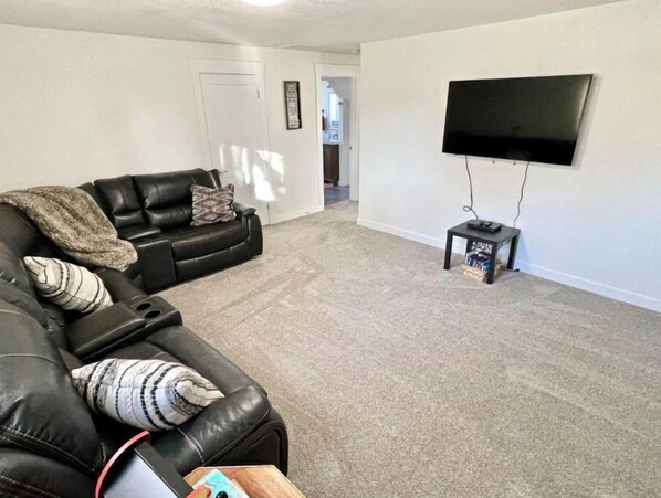 A living room with a black leather sofa, a flat-screen TV mounted on the wall, and a small table with a remote control. - Hometown USA With Hot Tub and Fully Renovated (Mountain Home)