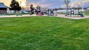 Un parque infantil con diversas estructuras de juego, incluyendo toboganes y zonas de escalada, con un cielo despejado y un atardecer de fondo.