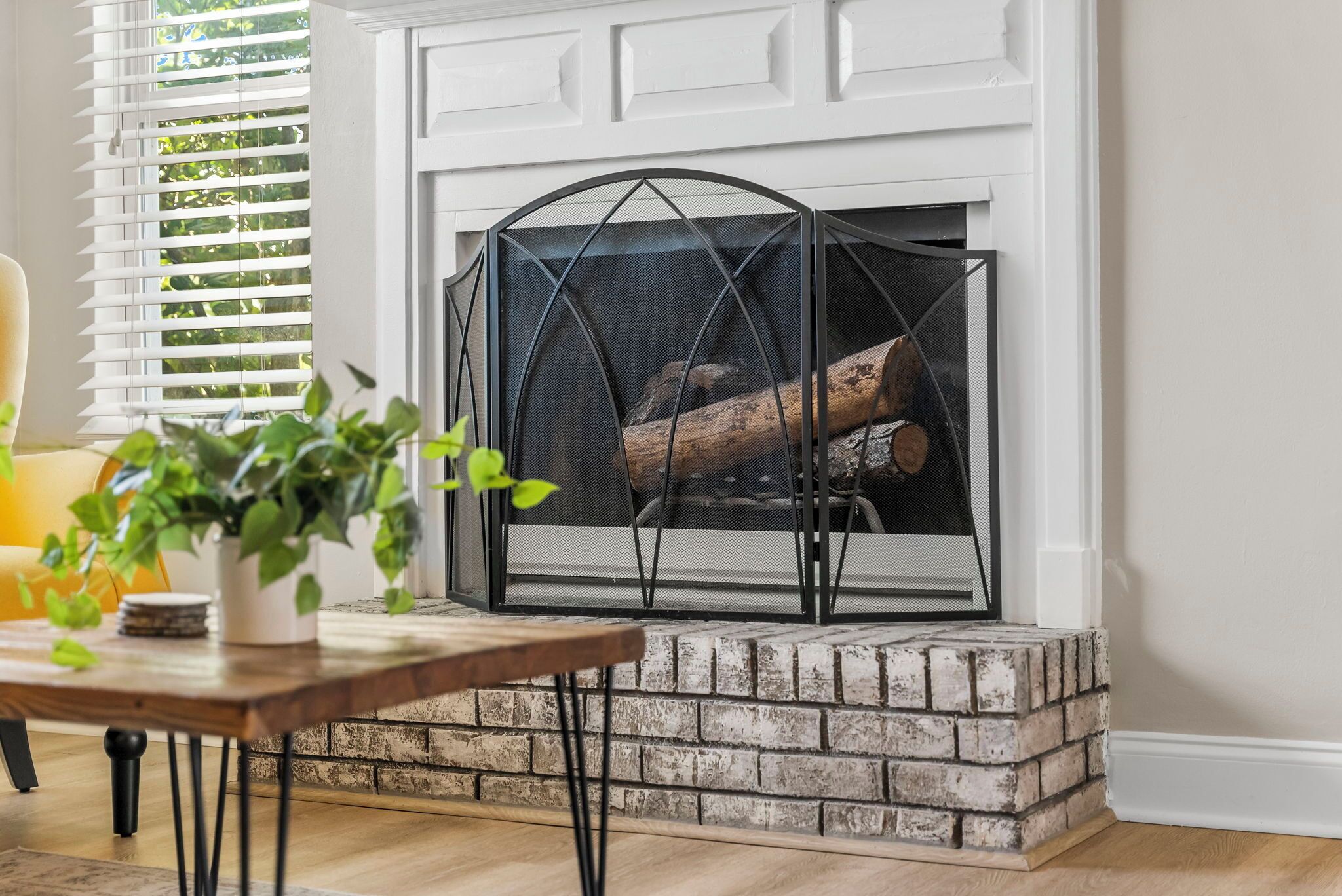 A fireplace with a white mantel and a black metal screen, surrounded by a brick base.