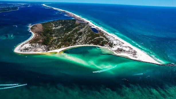 Luchtbeeld van een kusteiland met helder turquoise water, zandstranden en weelderige begroeiing.